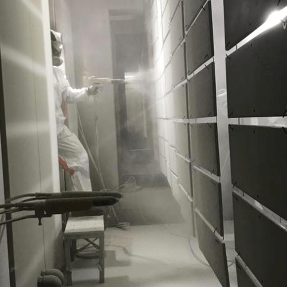 uomo con tuta bianca che vernicia a polvere dei pannelli di acciaio